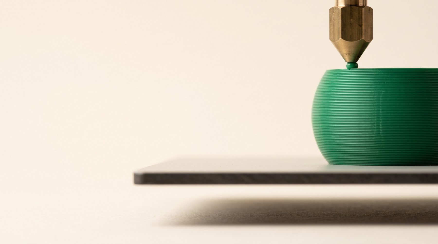 A 3D printer nozzle laying down a green object with visible layer lines